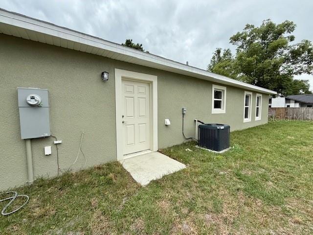 rear view of house with central air condition unit, stucco siding, and a lawn