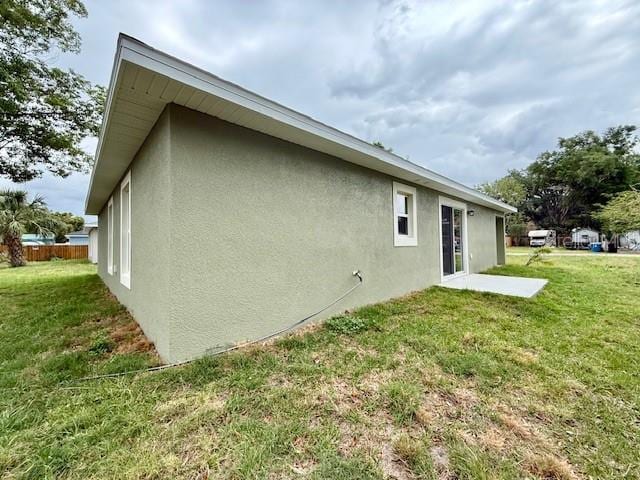 rear view of house featuring a lawn and stucco siding