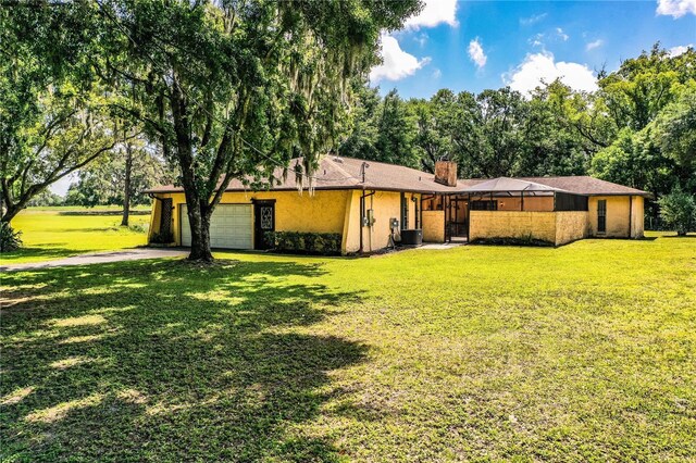 4101 N Forbes Rd, Plant City, FL 33565 - rear view of house featuring a garage, central AC unit, a lawn, driveway, and a chimney