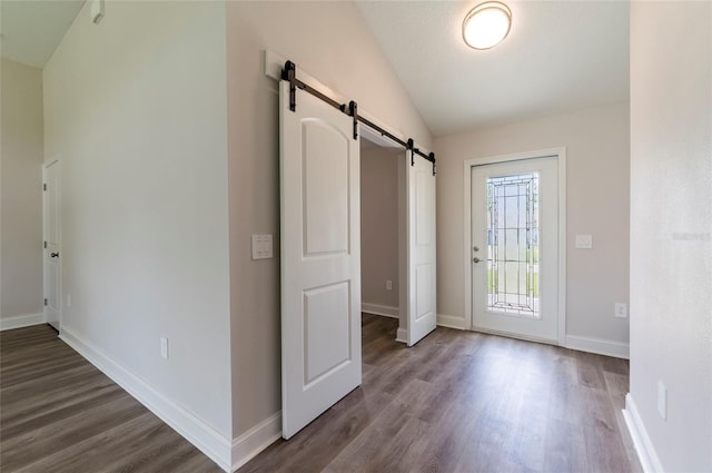 foyer with dark wood-type flooring, baseboards, a barn door, and vaulted ceiling