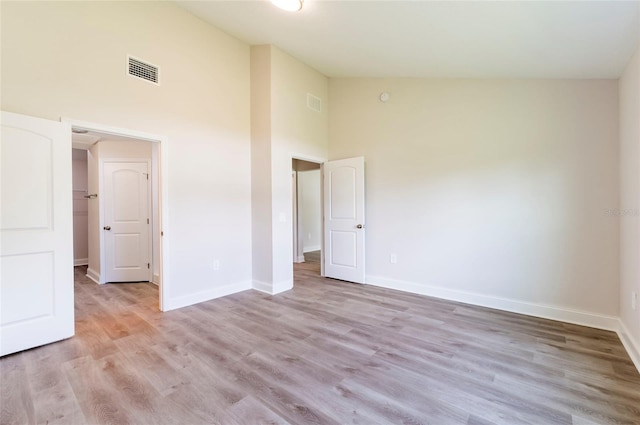 spare room featuring high vaulted ceiling, light wood finished floors, baseboards, and visible vents