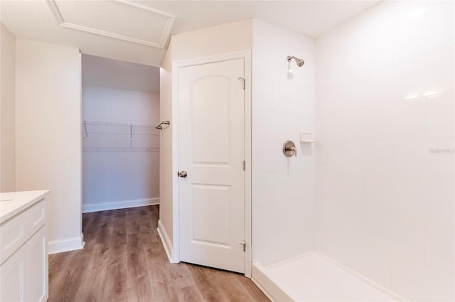 bathroom with tiled shower, vanity, wood finished floors, a walk in closet, and baseboards