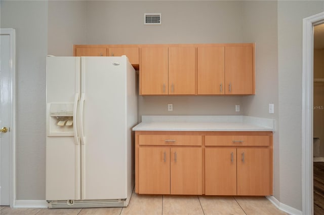 kitchen with white refrigerator with ice dispenser, light brown cabinetry, visible vents, light countertops, and baseboards