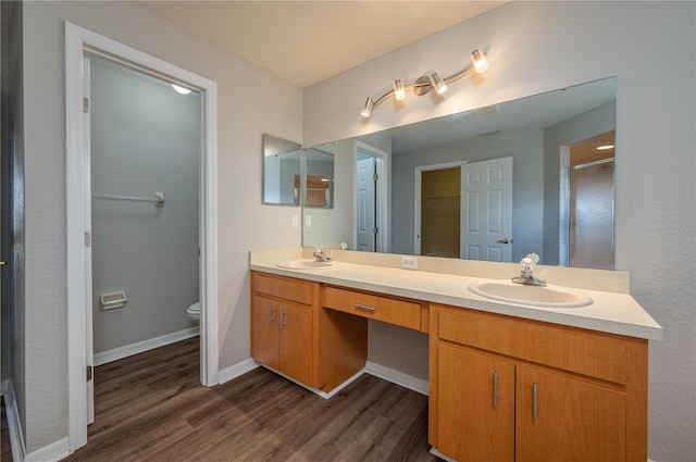 bathroom with double vanity, a sink, toilet, and wood finished floors