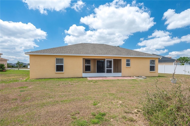 rear view of house featuring a yard, fence, a sunroom, and stucco siding