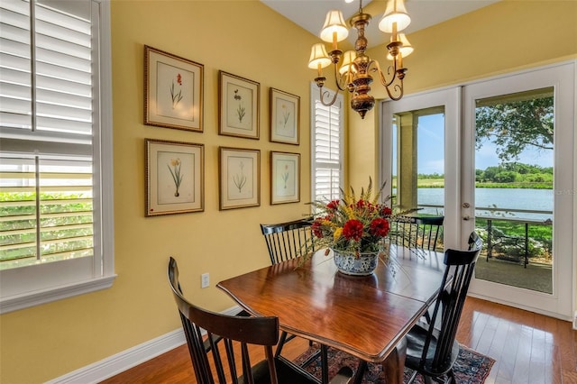 dining room with a water view, an inviting chandelier, french doors, wood-type flooring, and baseboards