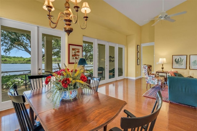 dining area featuring french doors, a water view, a towering ceiling, baseboards, and wood finished floors