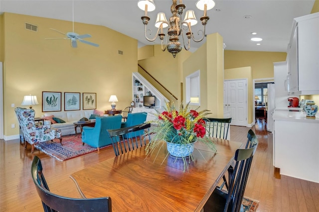 dining space featuring ceiling fan with notable chandelier, visible vents, high vaulted ceiling, and light wood-type flooring
