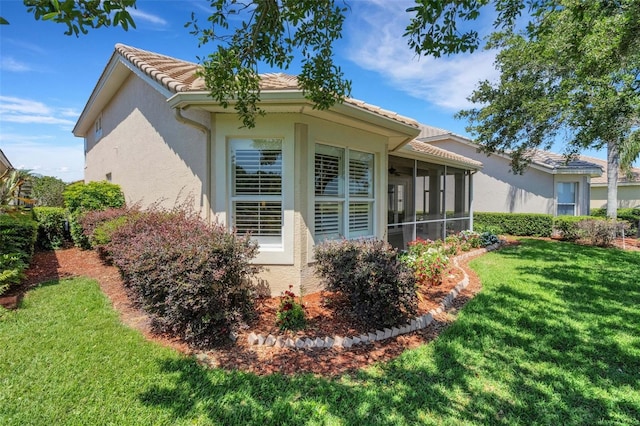 view of side of home with a tiled roof, a sunroom, a yard, and stucco siding