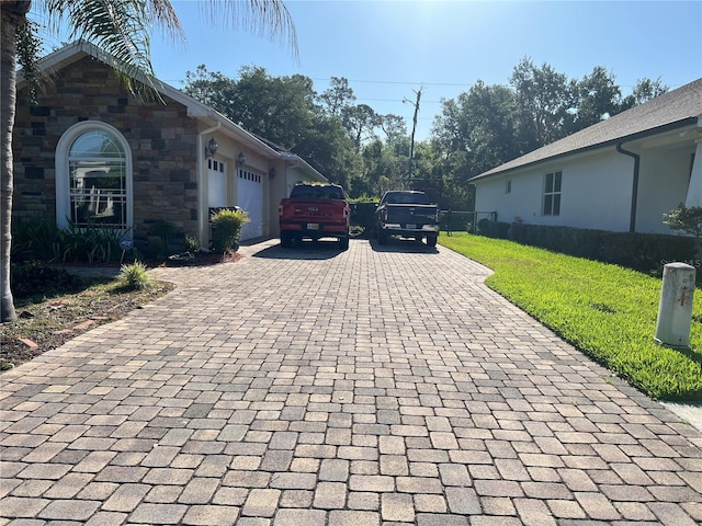 view of side of property with a garage, stone siding, decorative driveway, and a lawn