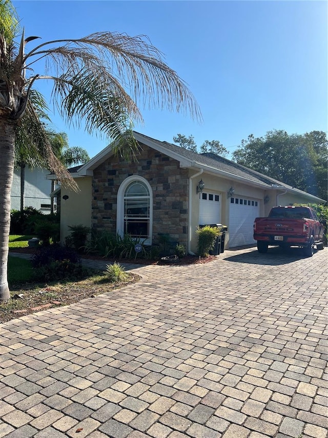 view of front of property featuring stone siding, a garage, decorative driveway, and stucco siding