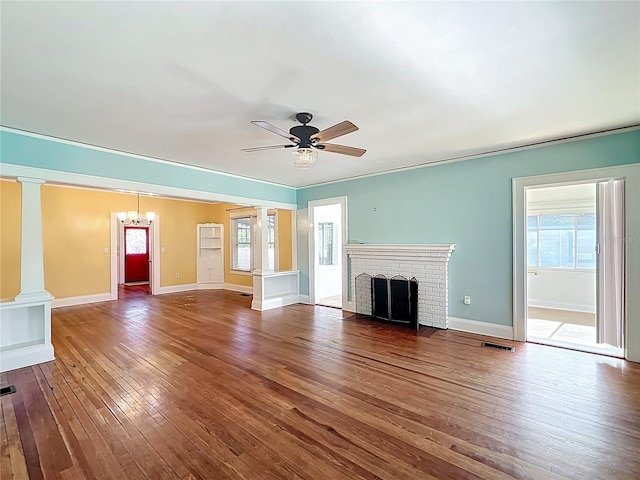 unfurnished living room with visible vents, baseboards, decorative columns, ceiling fan with notable chandelier, and wood-type flooring