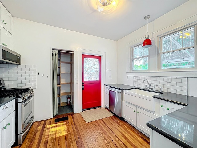 kitchen with a sink, dark countertops, light wood-style floors, stainless steel appliances, and backsplash