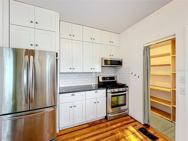kitchen featuring white cabinets, dark countertops, appliances with stainless steel finishes, light wood finished floors, and backsplash