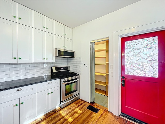 kitchen with light wood-type flooring, backsplash, dark countertops, white cabinets, and appliances with stainless steel finishes