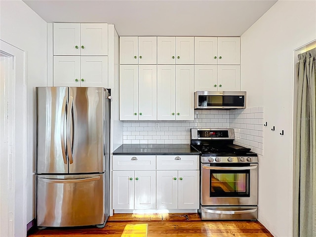 kitchen featuring light wood-style flooring, tasteful backsplash, white cabinets, appliances with stainless steel finishes, and dark countertops