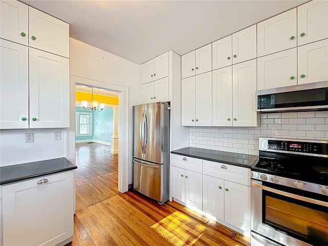 kitchen featuring tasteful backsplash, appliances with stainless steel finishes, a chandelier, white cabinetry, and light wood finished floors