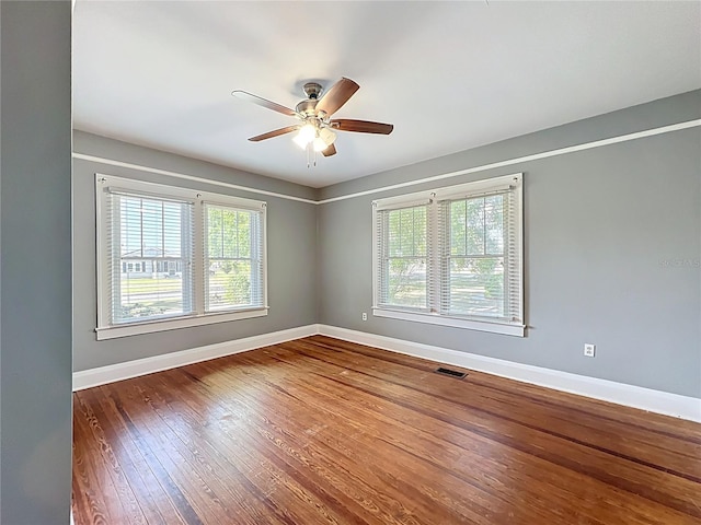 empty room with dark wood-type flooring, baseboards, a ceiling fan, and visible vents