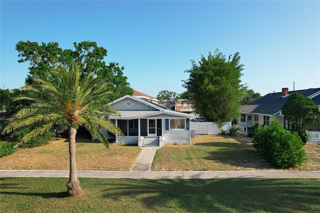 bungalow-style house with a front lawn, fence, and a sunroom