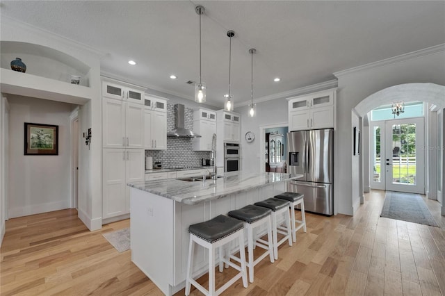 9004 Selph Rd, Lakeland, FL 33810 - kitchen featuring arched walkways, wall chimney exhaust hood, ornamental molding, light wood-type flooring, and stainless steel appliances