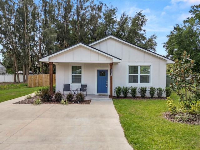 view of front of house featuring a porch, board and batten siding, fence, and a front lawn