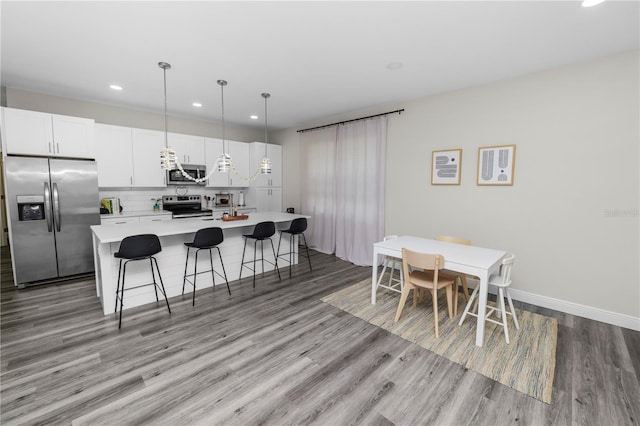 kitchen featuring light wood-type flooring, a breakfast bar, recessed lighting, a center island with sink, and stainless steel appliances
