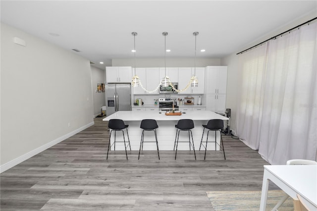kitchen featuring a kitchen breakfast bar, an island with sink, light countertops, white cabinets, and stainless steel appliances