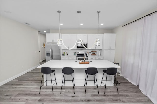 kitchen with a breakfast bar, white cabinets, a kitchen island with sink, visible vents, and stainless steel appliances