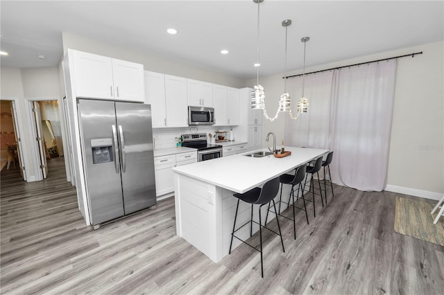 kitchen featuring a kitchen breakfast bar, light wood-type flooring, white cabinetry, appliances with stainless steel finishes, and a sink