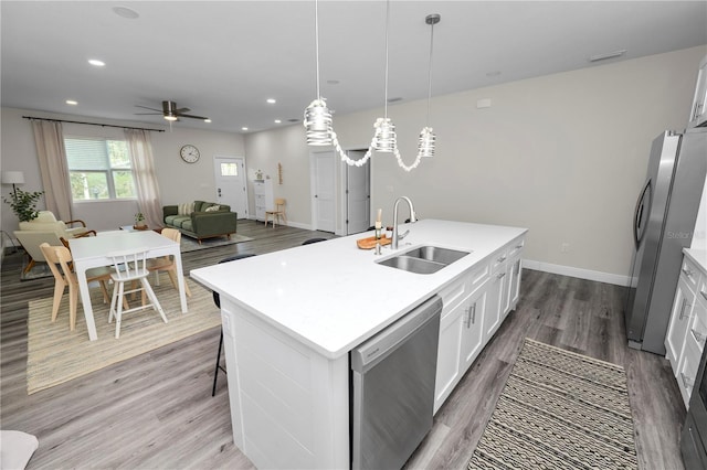 kitchen featuring white cabinets, a sink, open floor plan, wood finished floors, and stainless steel appliances