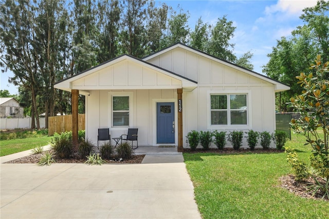view of front of property featuring board and batten siding, a front yard, fence, and covered porch