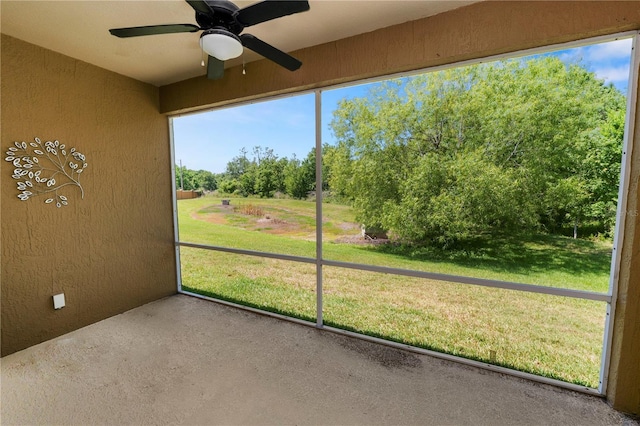 unfurnished sunroom featuring ceiling fan and view of wooded area