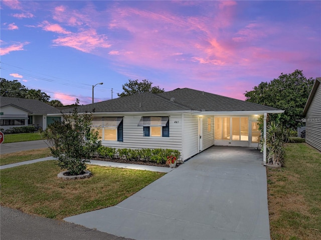 ranch-style home featuring concrete driveway, a yard, roof with shingles, and a carport