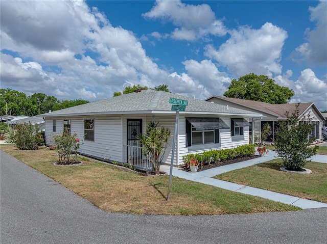 ranch-style home featuring covered porch, roof with shingles, and a front yard