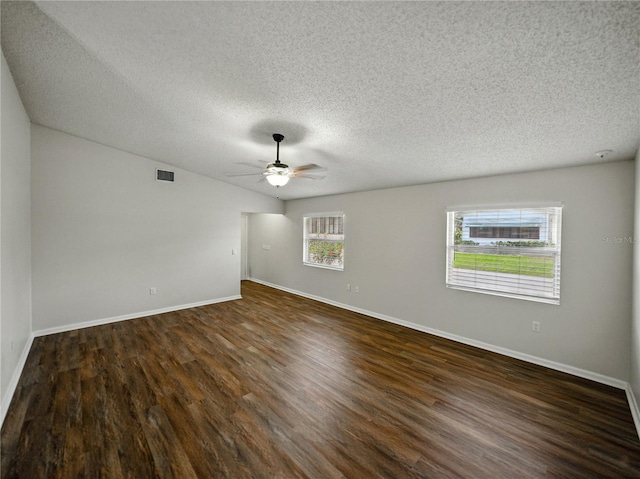 empty room featuring a textured ceiling, dark wood-type flooring, visible vents, ceiling fan, and baseboards