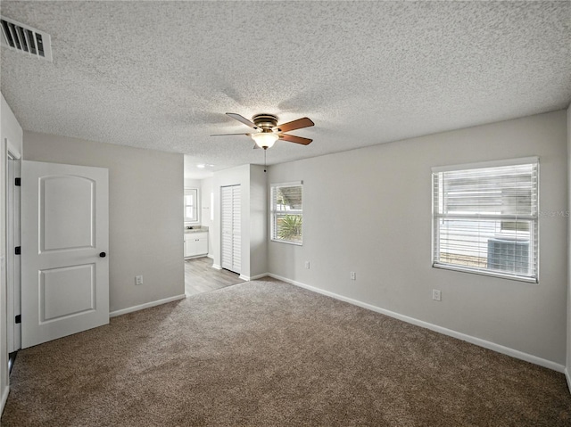 unfurnished bedroom featuring a textured ceiling, baseboards, ensuite bathroom, carpet flooring, and visible vents