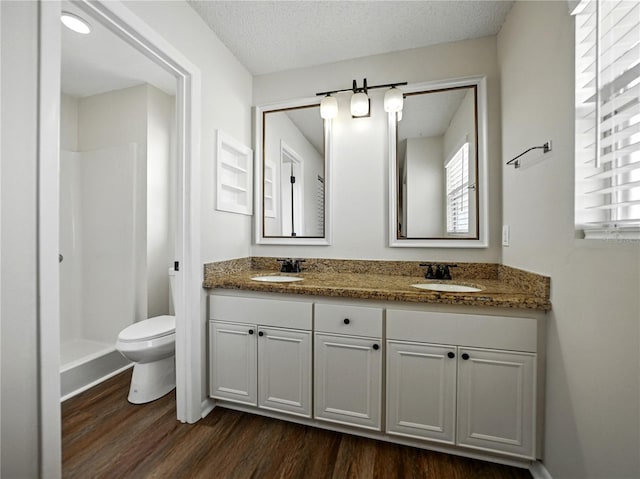 full bath with toilet, double vanity, a sink, and wood finished floors