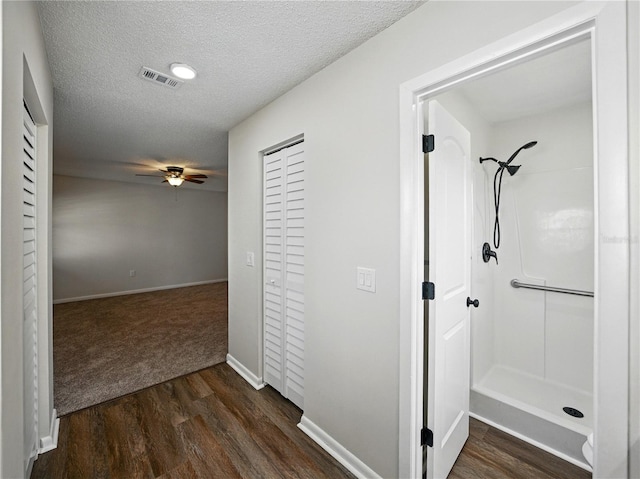 hall featuring a textured ceiling, baseboards, visible vents, and dark wood finished floors
