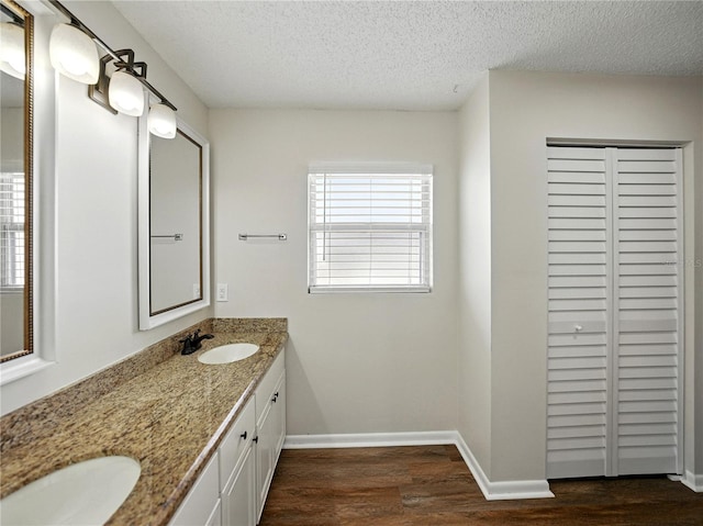 bathroom with double vanity, wood finished floors, a sink, a textured ceiling, and baseboards
