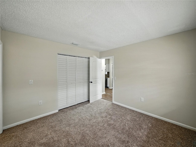 unfurnished bedroom with a closet, a textured ceiling, visible vents, carpet floors, and baseboards
