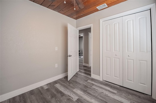 unfurnished bedroom with a closet, visible vents, wood ceiling, wood finished floors, and baseboards