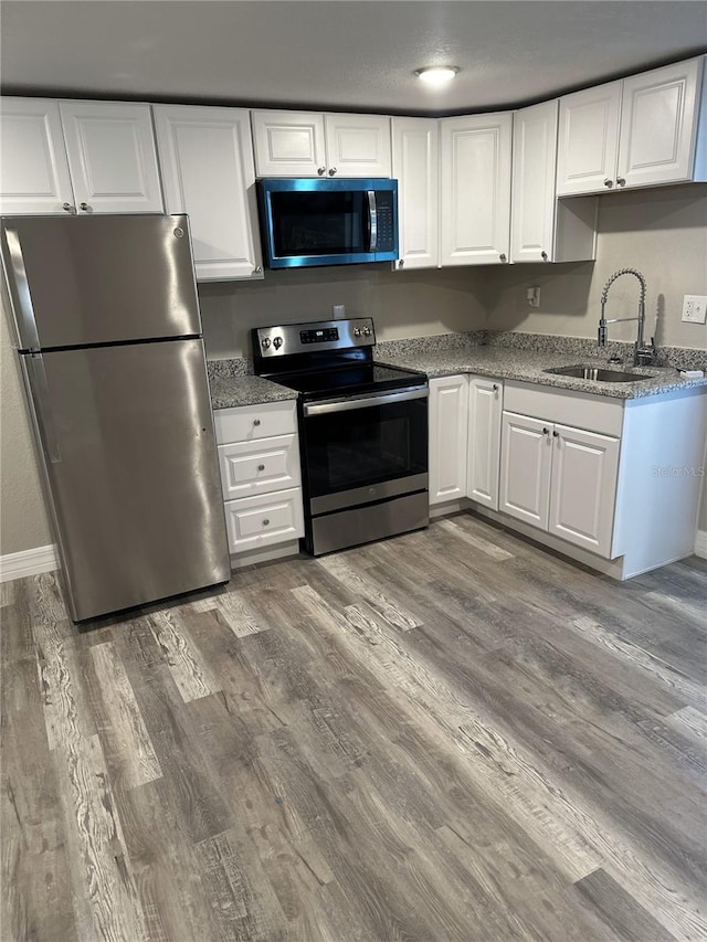 kitchen with wood finished floors, white cabinets, a sink, and appliances with stainless steel finishes