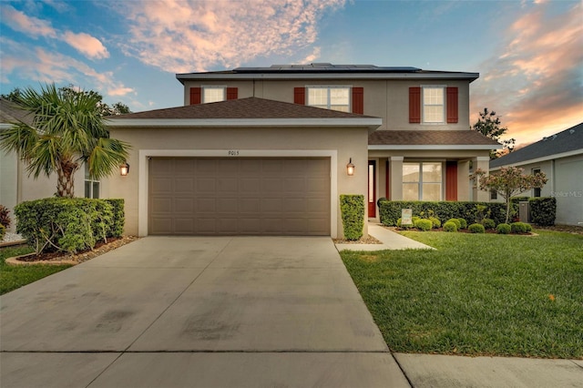 traditional-style house featuring a front lawn, concrete driveway, an attached garage, roof mounted solar panels, and stucco siding