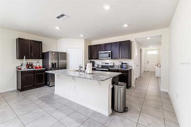 kitchen featuring an island with sink, stainless steel appliances, visible vents, light tile patterned floors, and a kitchen bar