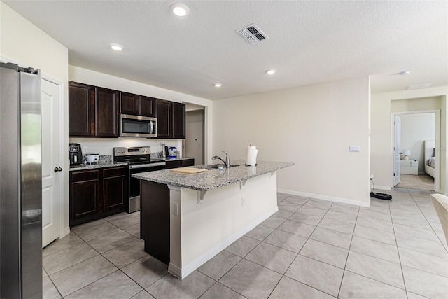kitchen with stainless steel appliances, a sink, a center island with sink, light tile patterned flooring, and visible vents