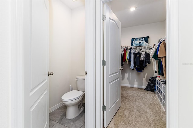 bathroom with a spacious closet, toilet, and baseboards