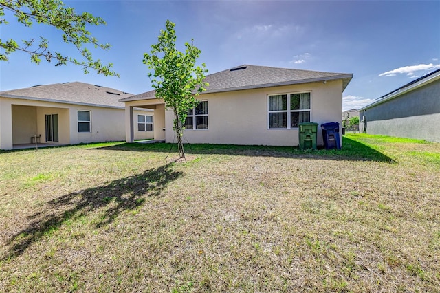 back of property with a lawn, a shingled roof, and stucco siding