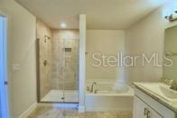 bathroom with vanity, baseboards, a shower stall, and a garden tub