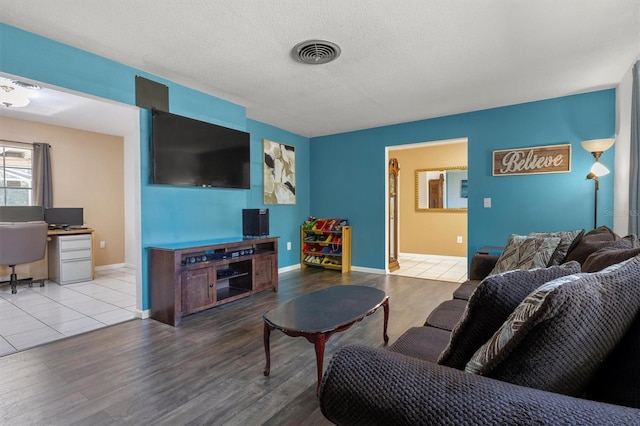 living room featuring a textured ceiling, wood finished floors, baseboards, and visible vents