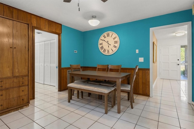dining room with wooden walls, light tile patterned flooring, a wainscoted wall, and ceiling fan